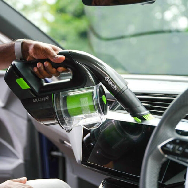  Man vacuuming car air vents and infotainment screens using Gtech Multi K9’s small upholstery brush attachment to prevent scratches.