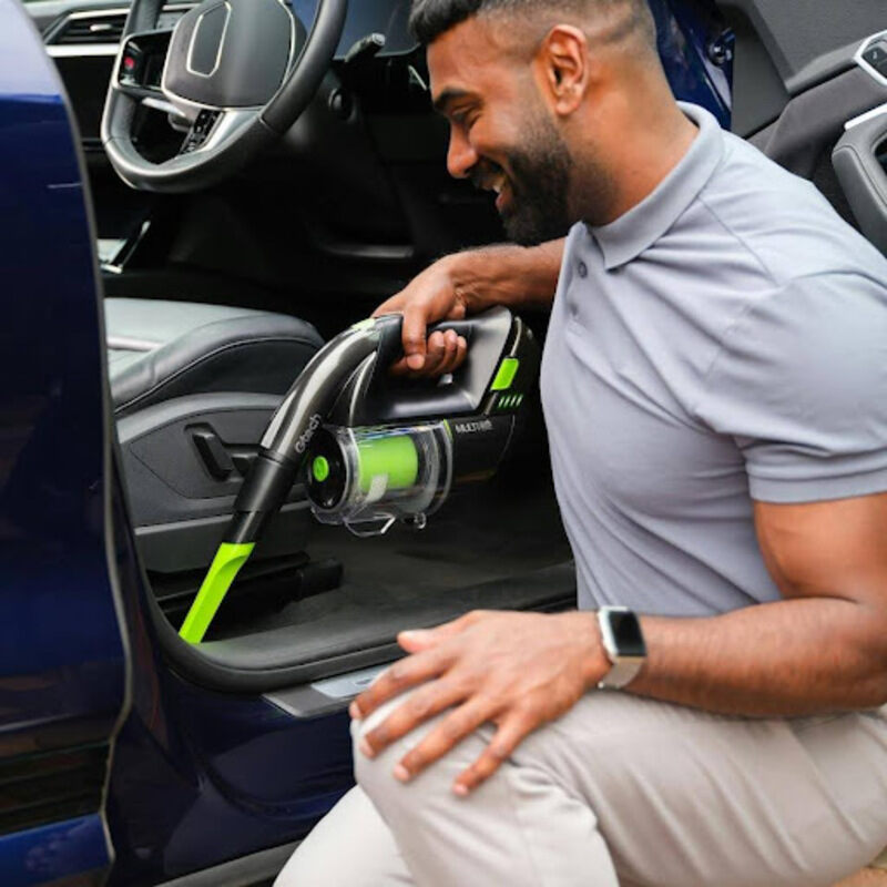 Man using Gtech Multi handheld vacuum’s slim crevice tool to clean deep between car seats and seat rails.
